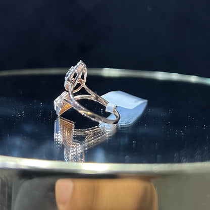 Elegant open-style diamond ring featuring a pear-shaped halo on one side and a square cluster on the other, worn in a black mannequin's hand displayed displayed against a reflective metallic background.
