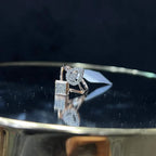 Elegant open-style diamond ring featuring a pear-shaped halo on one side and a square cluster on the other, worn in a black mannequin's hand displayed displayed against a reflective metallic background.