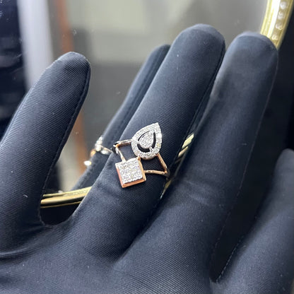 Elegant open-style diamond ring featuring a pear-shaped halo on one side and a square cluster on the other, worn in a black mannequin's hand displayed displayed against a reflective metallic background.