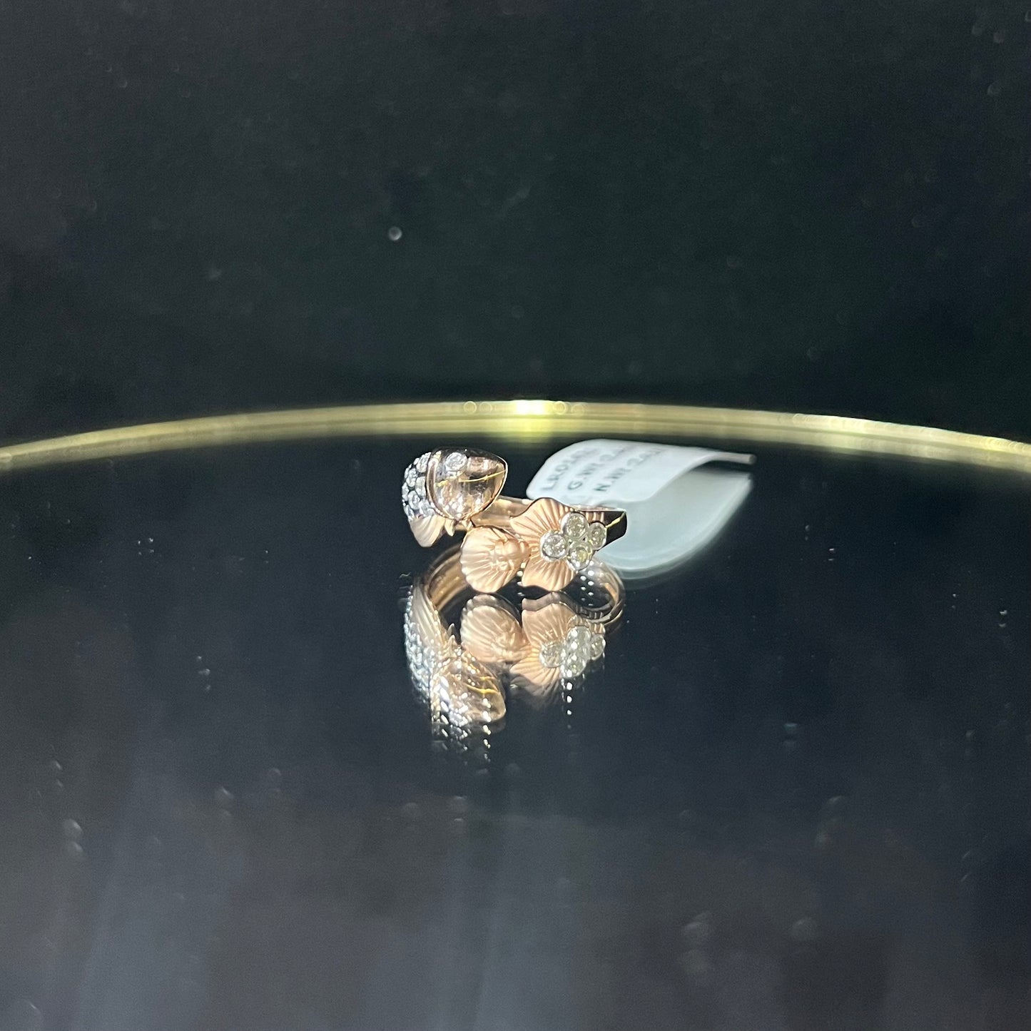 A ring with a gold band and a central natural diamonds, displayed on a reflective surface.
