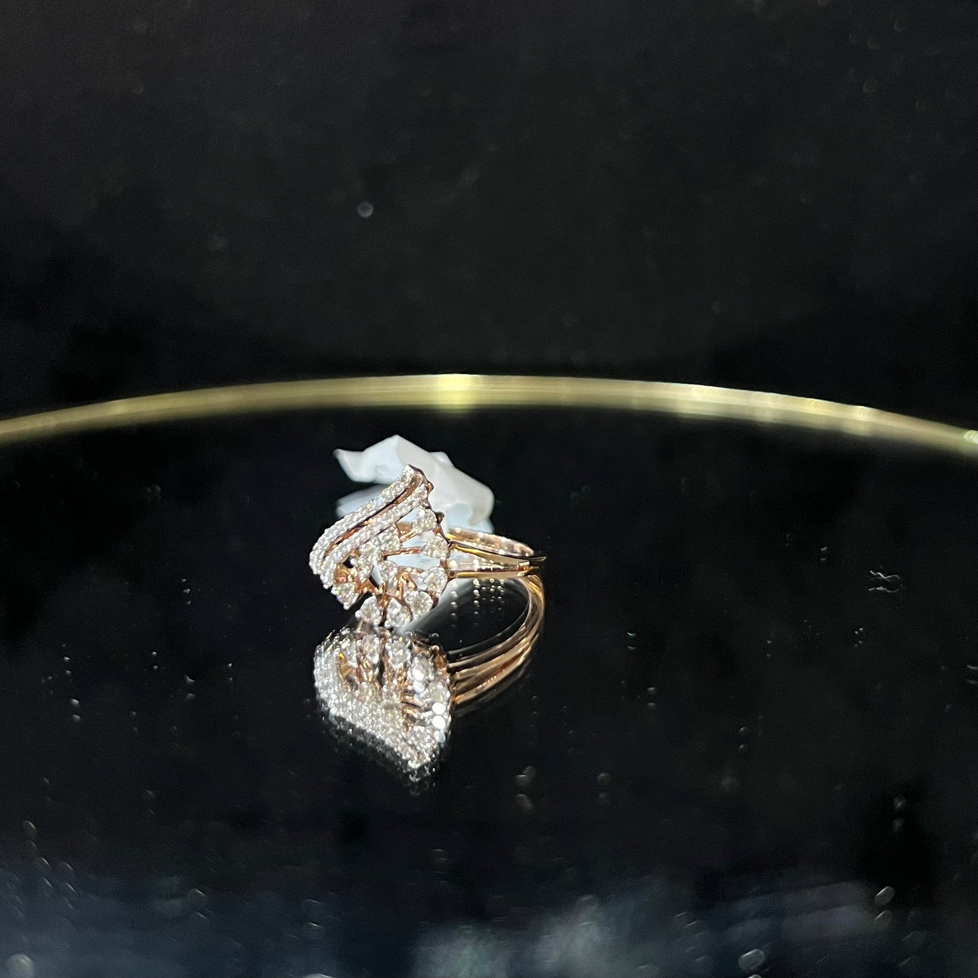 A handcrafted natural diamond solid gold ring displayed on a reflective surface, with a brilliant cut diamond in a gold band.