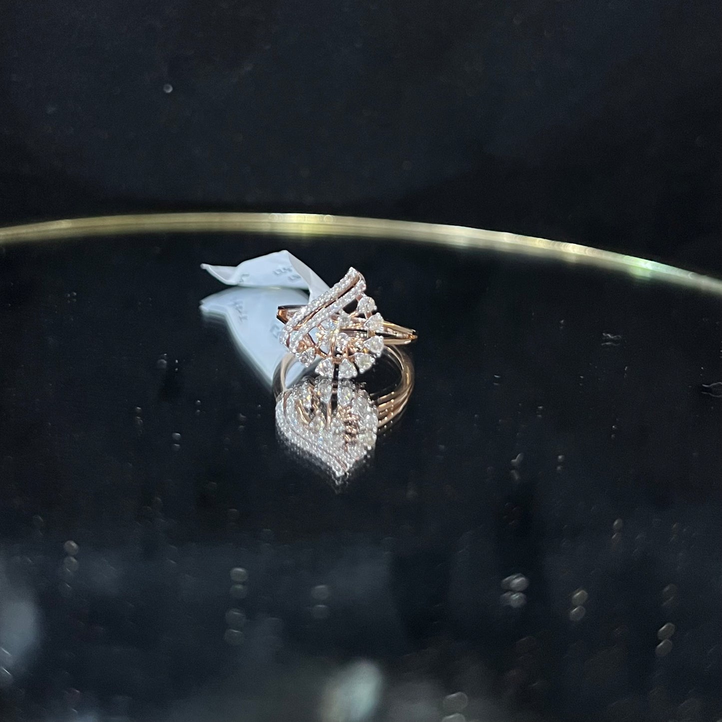 A handcrafted natural diamond solid gold ring displayed on a reflective surface, with a brilliant cut diamond in a gold band.
