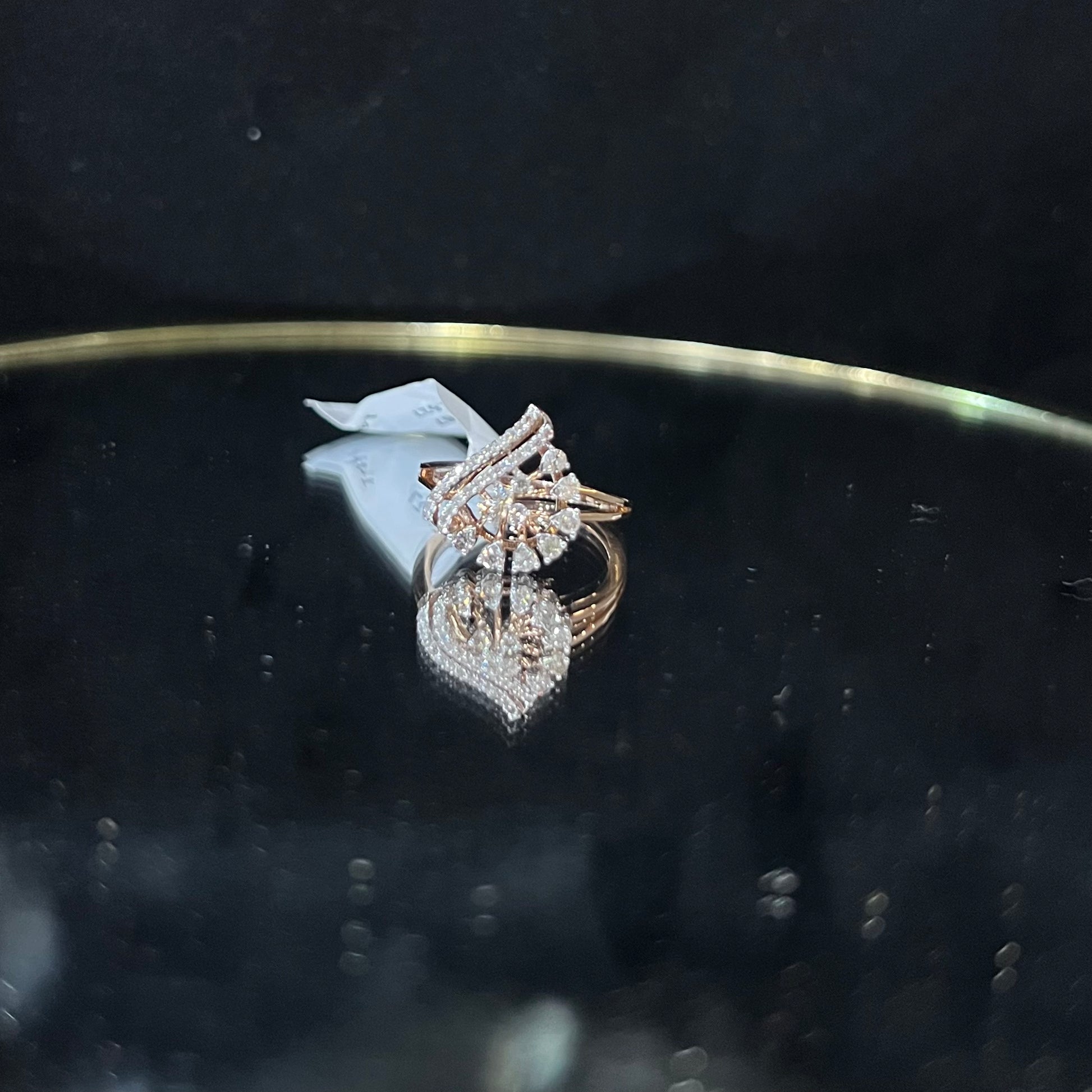A handcrafted natural diamond solid gold ring displayed on a reflective surface, with a brilliant cut diamond in a gold band.