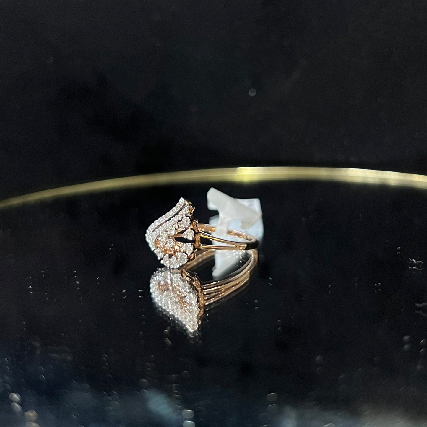 A handcrafted natural diamond solid gold ring displayed on a reflective surface, with a brilliant cut diamond in a gold band.