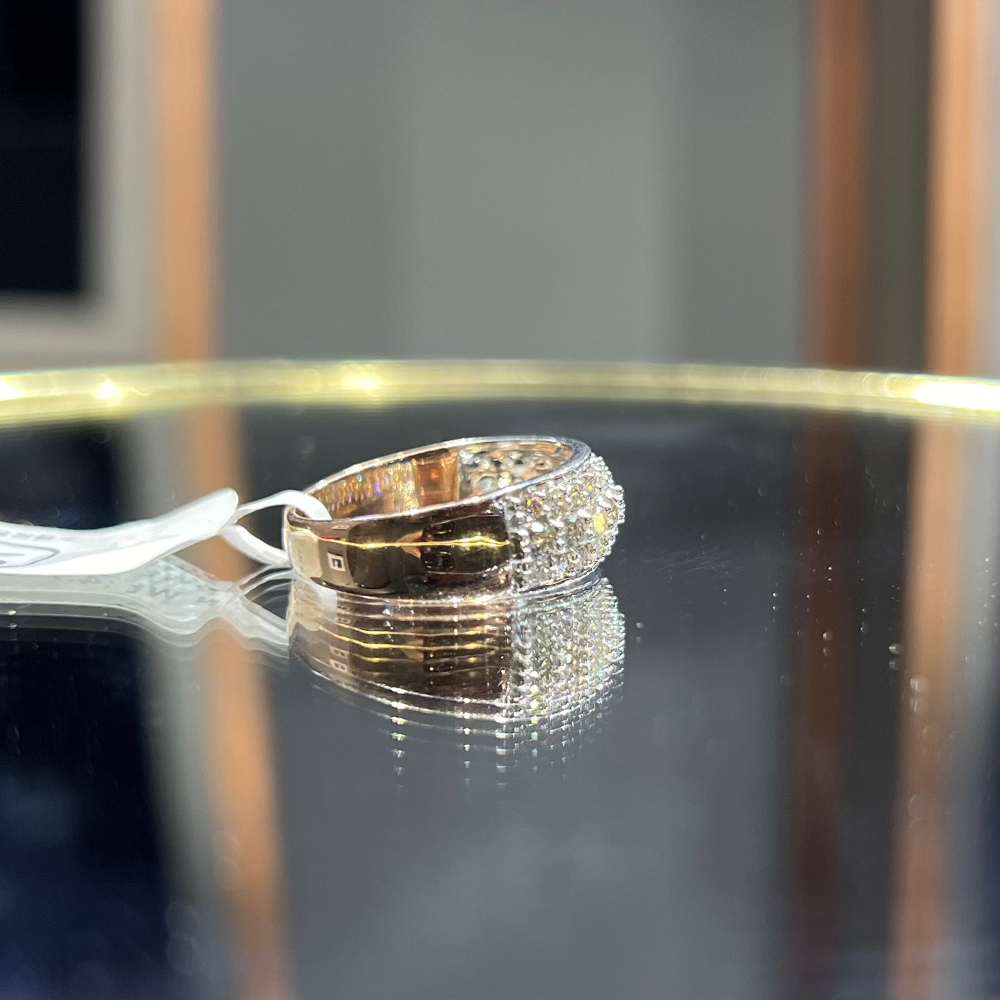 Close-up of a wide diamond band ring, featuring multiple rows of sparkling round-cut diamonds set in gold, displayed on a reflective surface.