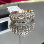 Close-up of a wide diamond band ring, featuring multiple rows of sparkling round-cut diamonds set in gold, displayed on a reflective surface.