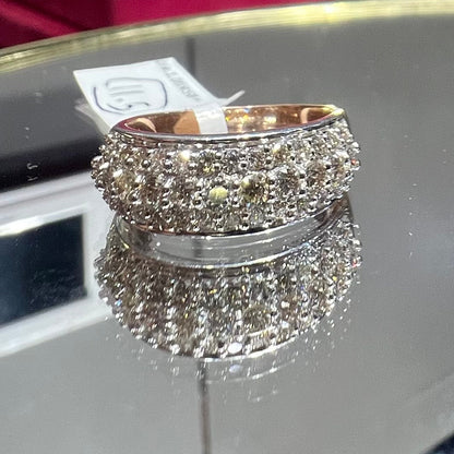 Close-up of a wide diamond band ring, featuring multiple rows of sparkling round-cut diamonds set in gold, displayed on a reflective surface.