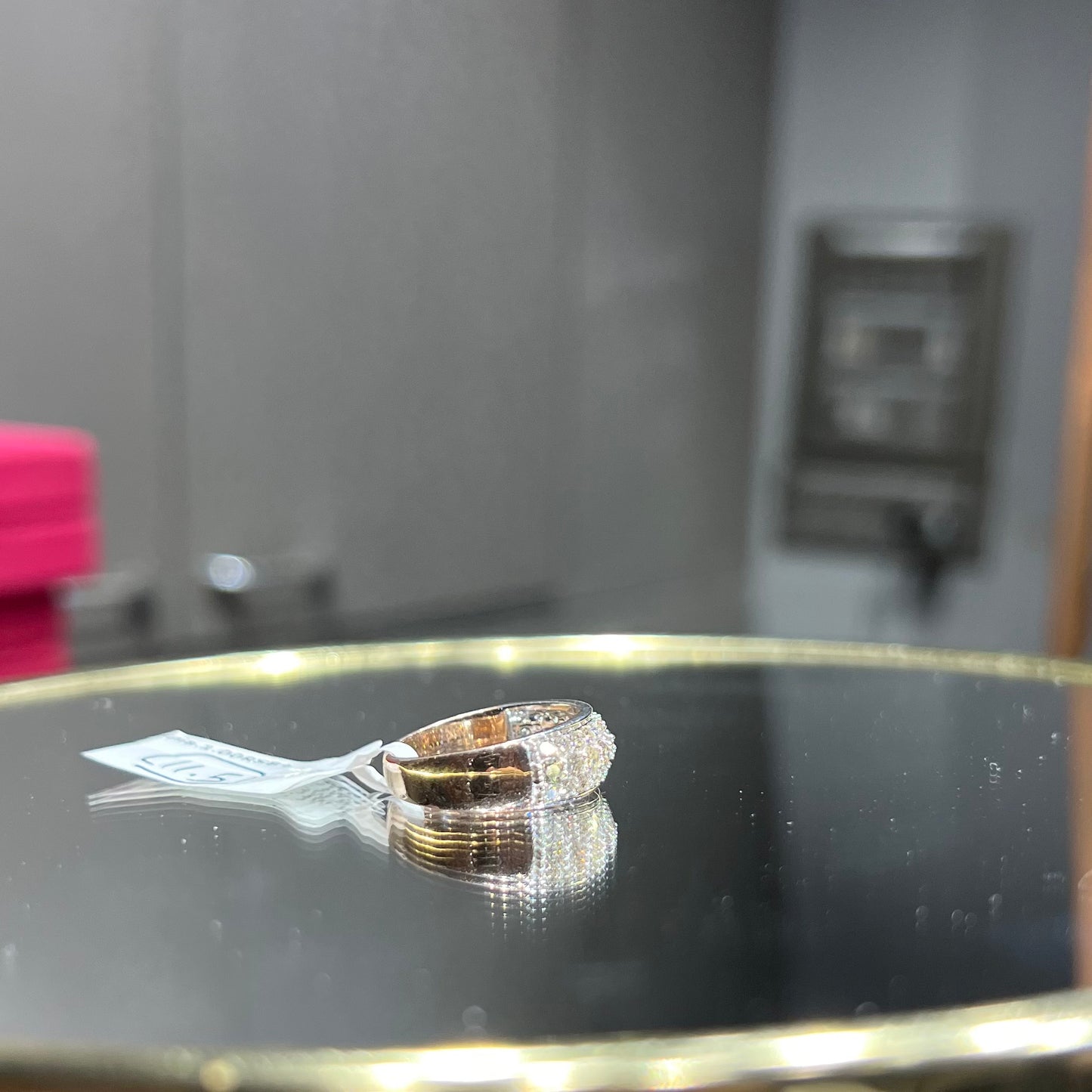 Close-up of a wide diamond band ring, featuring multiple rows of sparkling round-cut diamonds set in gold, displayed on a reflective surface.