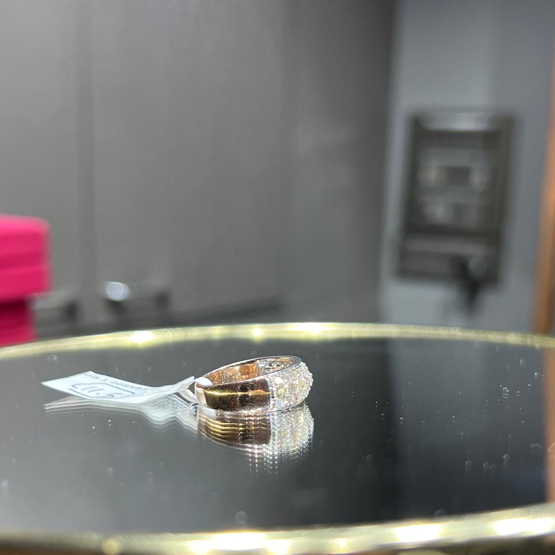 Close-up of a wide diamond band ring, featuring multiple rows of sparkling round-cut diamonds set in gold, displayed on a reflective surface.