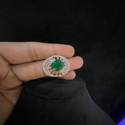 Close-up of a hand holding an elegant statement ring featuring a large oval green gemstone at the center, surrounded by concentric circles of sparkling white diamonds set in a gold base against a black background.