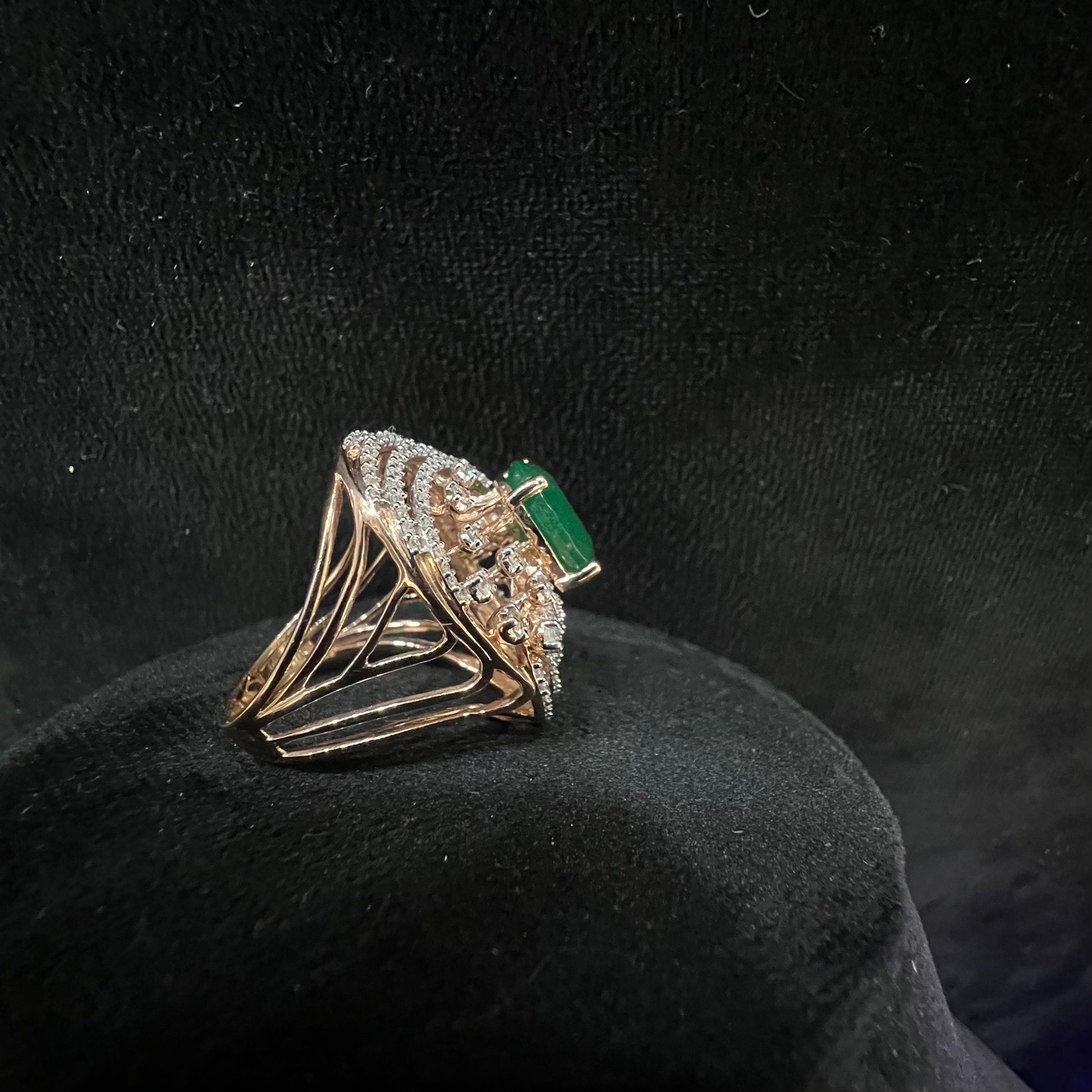 Close-up of an elegant statement ring featuring a large oval green gemstone at the center, surrounded by concentric circles of sparkling white diamonds set in a gold base against a black background.