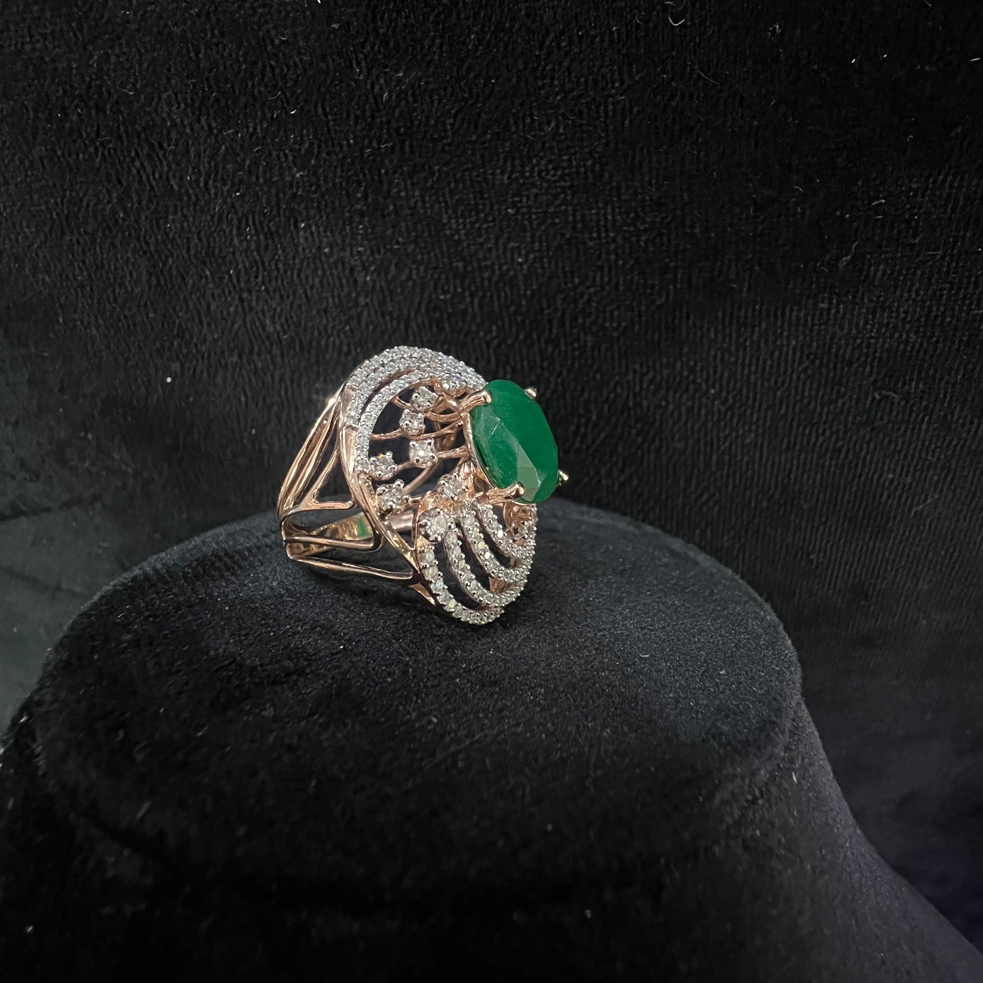 Close-up of an elegant statement ring featuring a large oval green gemstone at the center, surrounded by concentric circles of sparkling white diamonds set in a gold base against a black background.