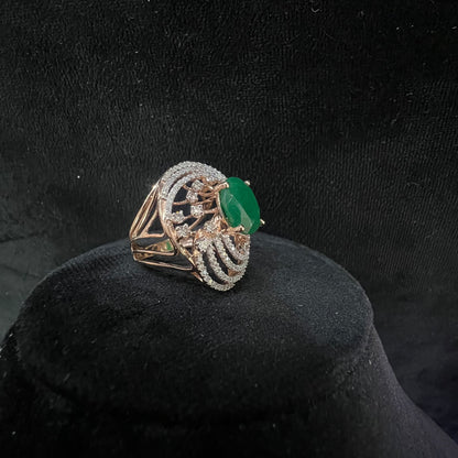 Close-up of an elegant statement ring featuring a large oval green gemstone at the center, surrounded by concentric circles of sparkling white diamonds set in a gold base against a black background.