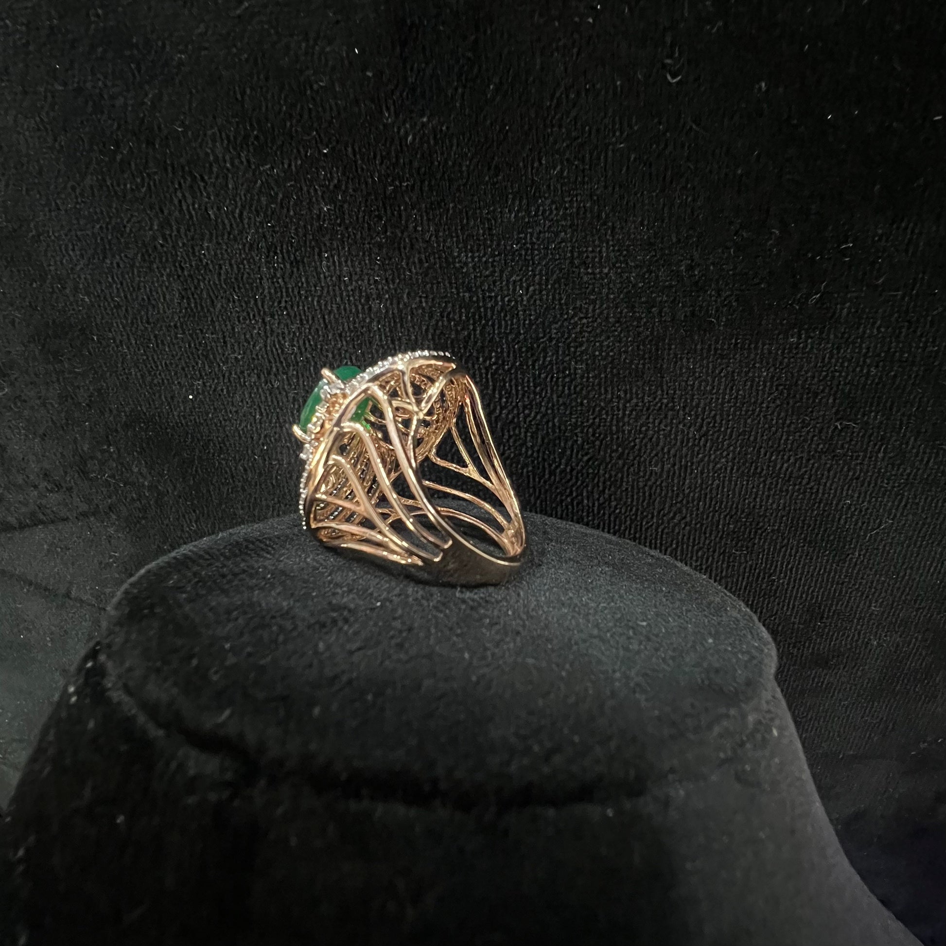 Close-up of an elegant statement ring featuring a large oval green gemstone at the center, surrounded by concentric circles of sparkling white diamonds set in a gold base against a black background.