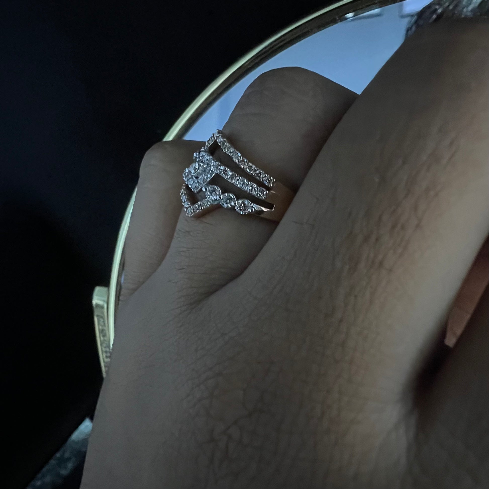 A person's hand displaying a gold band ring with central diamonds, surrounded by smaller diamonds set in the band.