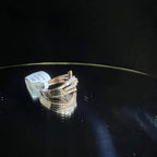 A gold band ring with central diamonds, surrounded by smaller diamonds set in the band is displayed on a reflective surface.
