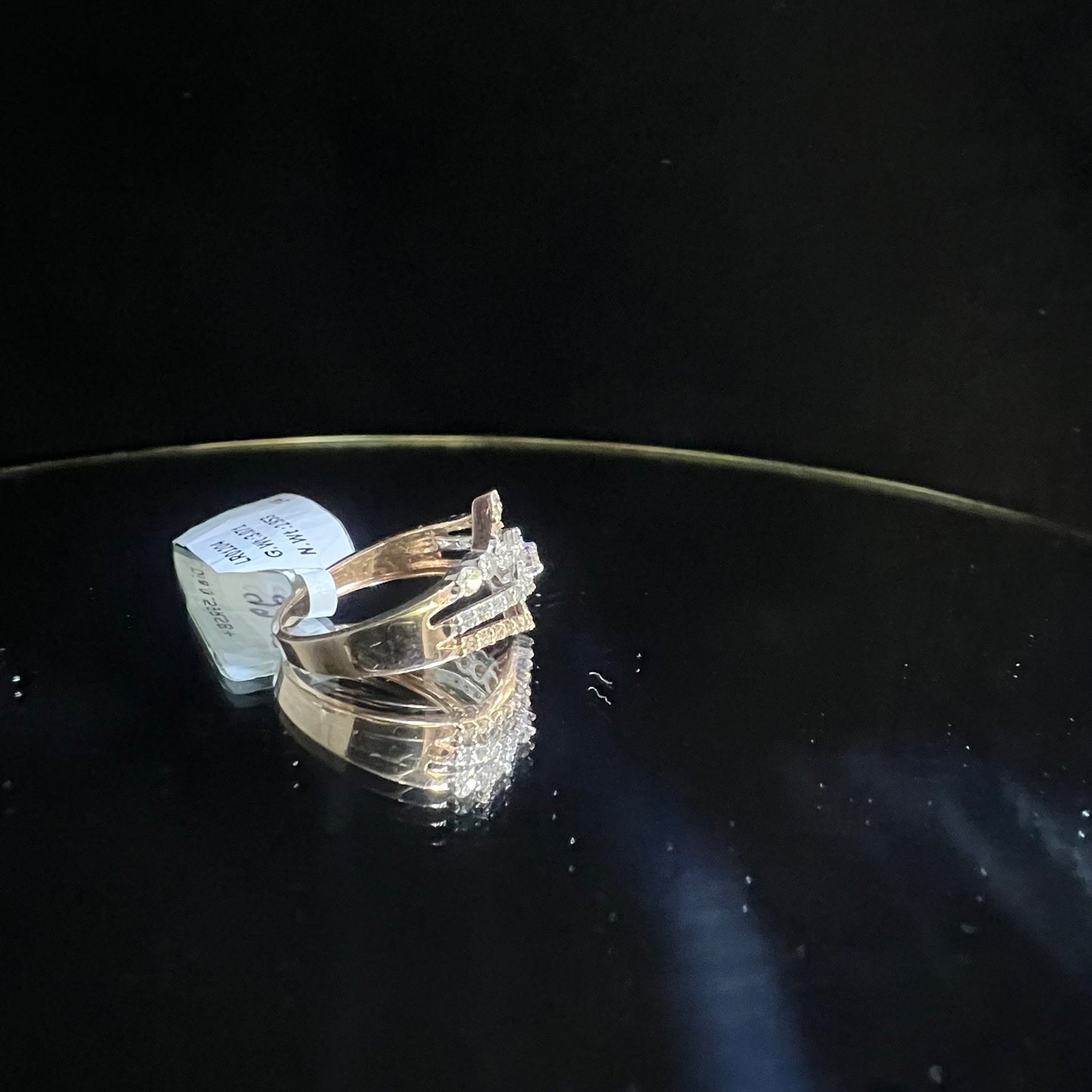 A gold band ring with central diamonds, surrounded by smaller diamonds set in the band is displayed on a reflective surface.