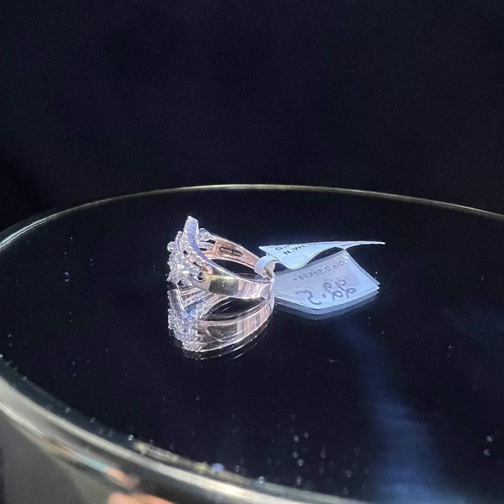 A gold band ring with central diamonds, surrounded by smaller diamonds set in the band is displayed on a reflective surface.