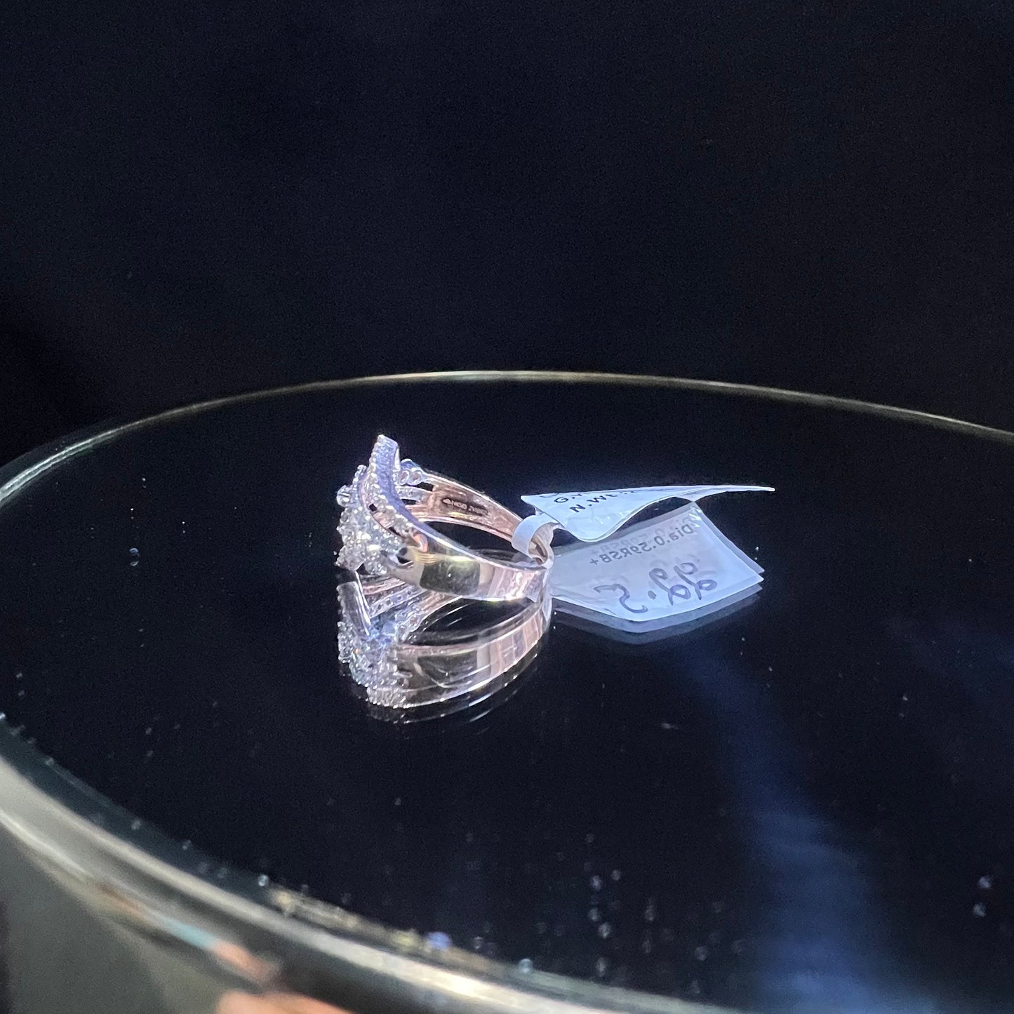 A gold band ring with central diamonds, surrounded by smaller diamonds set in the band is displayed on a reflective surface.