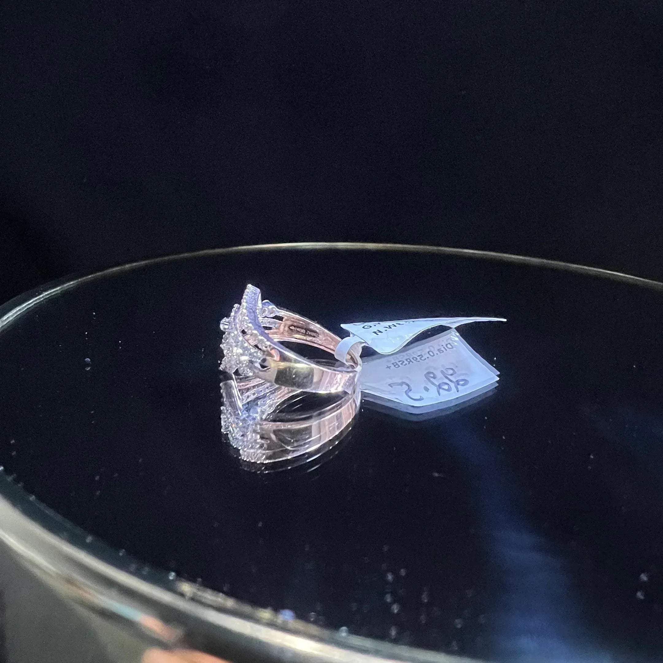 A gold band ring with central diamonds, surrounded by smaller diamonds set in the band is displayed on a reflective surface.