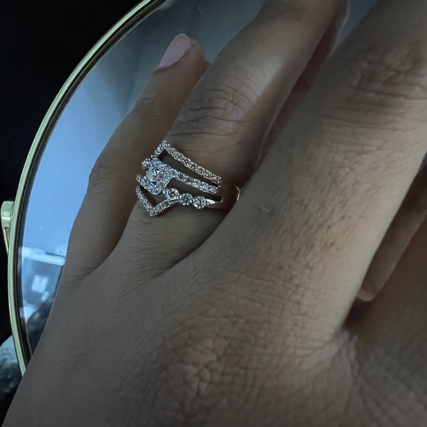 A person's hand displaying a gold band ring with central diamonds, surrounded by smaller diamonds set in the band.