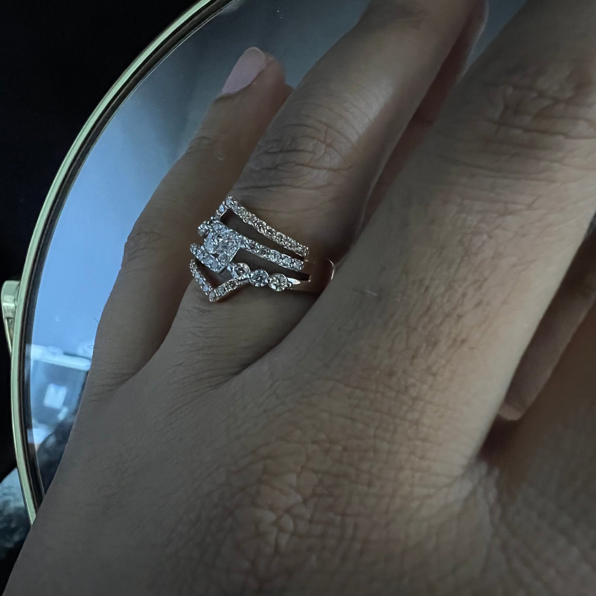 A person's hand displaying a gold band ring with central diamonds, surrounded by smaller diamonds set in the band.