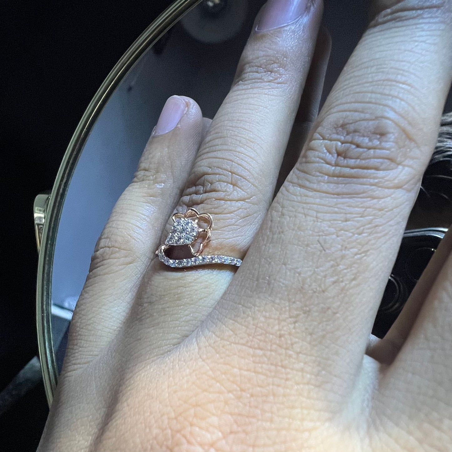 A person's hand displaying a gold band ring with a central natural diamond, surrounded by smaller clear stones.