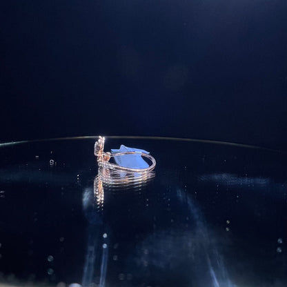 A gold band ring with a central natural diamond, surrounded by smaller clear stones displayed on a reflective surface.