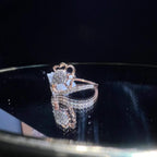 A gold band ring with a central natural diamond, surrounded by smaller clear stones displayed on a reflective surface.