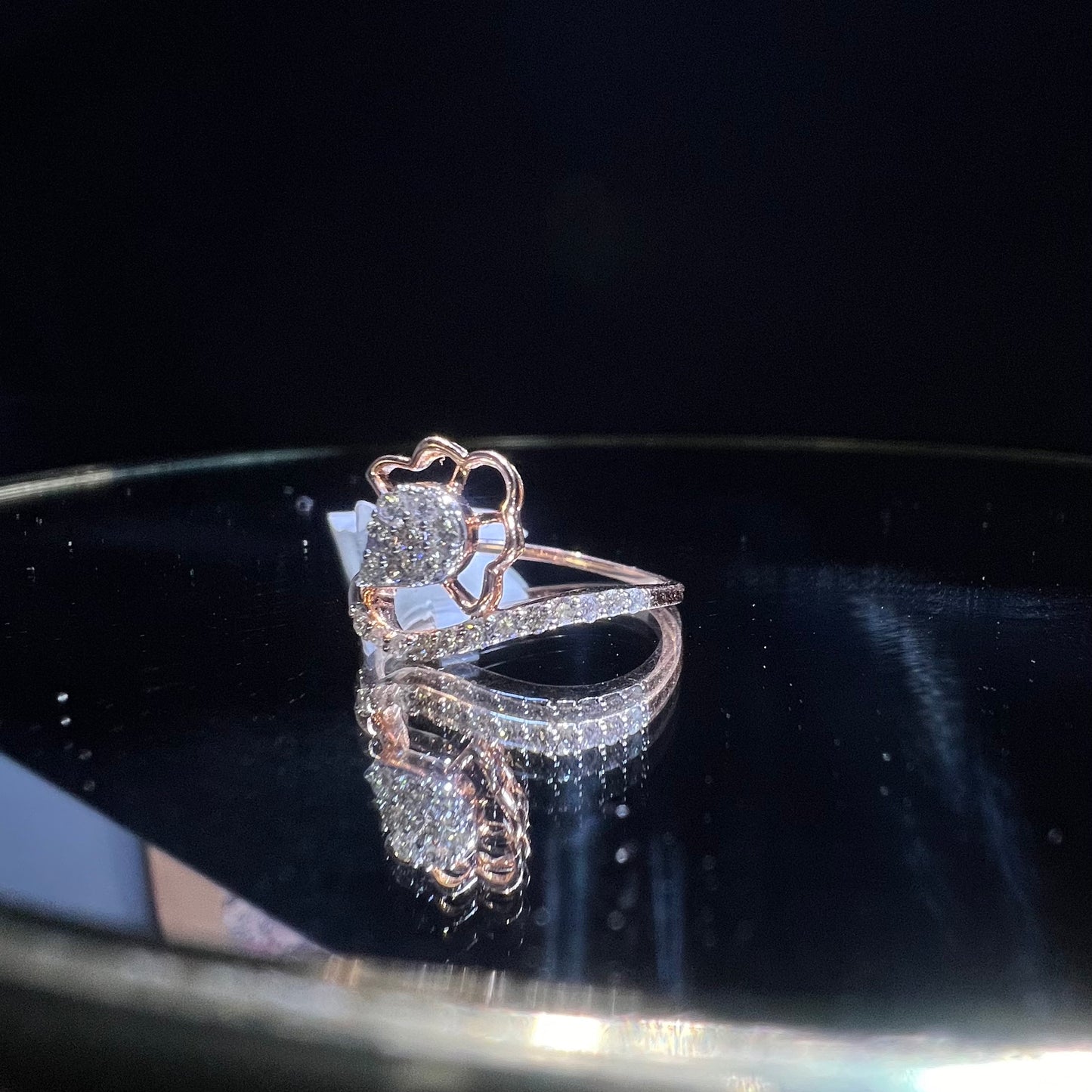 A gold band ring with a central natural diamond, surrounded by smaller clear stones displayed on a reflective surface.