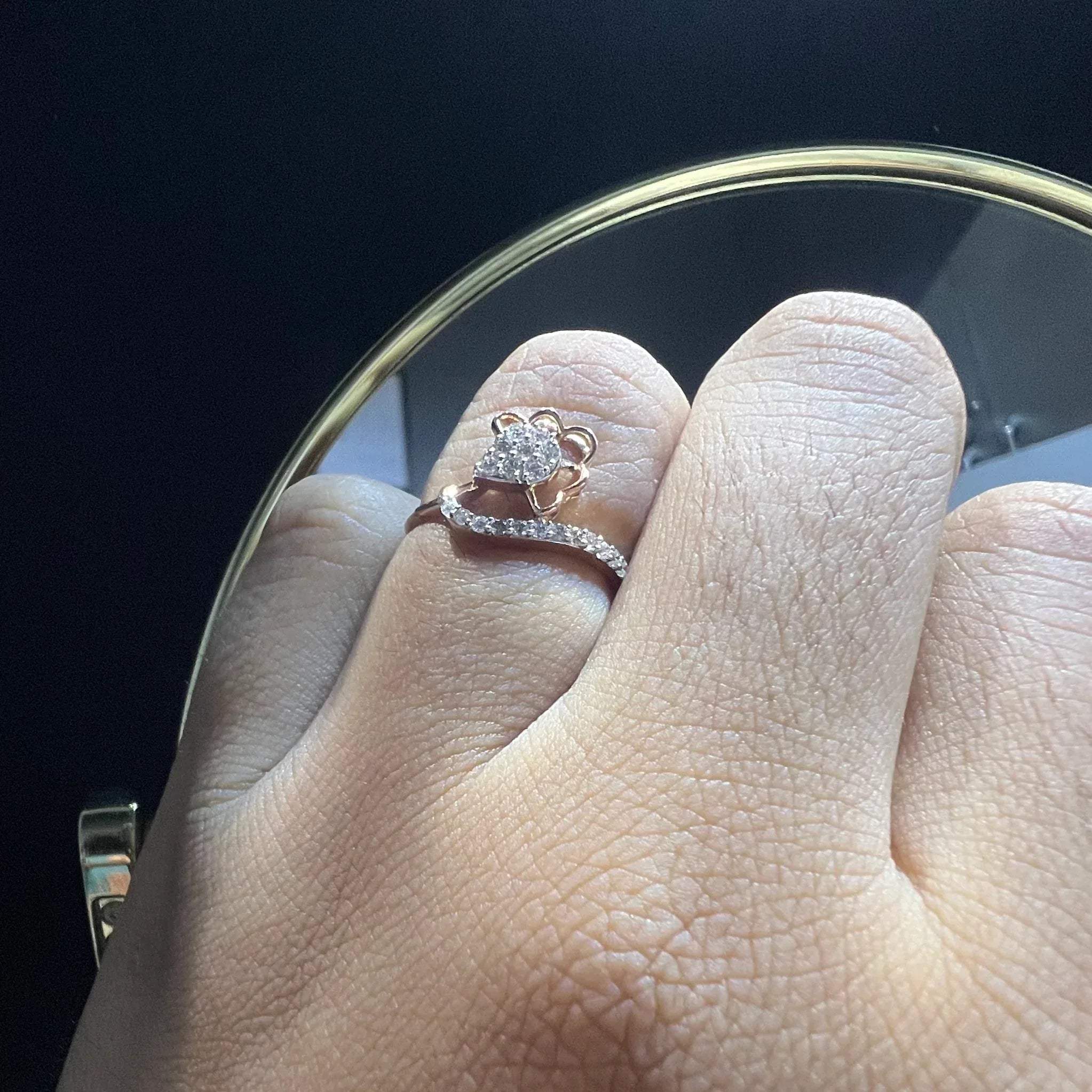 A person's hand displaying a gold band ring with a central natural diamond, surrounded by smaller clear stones.