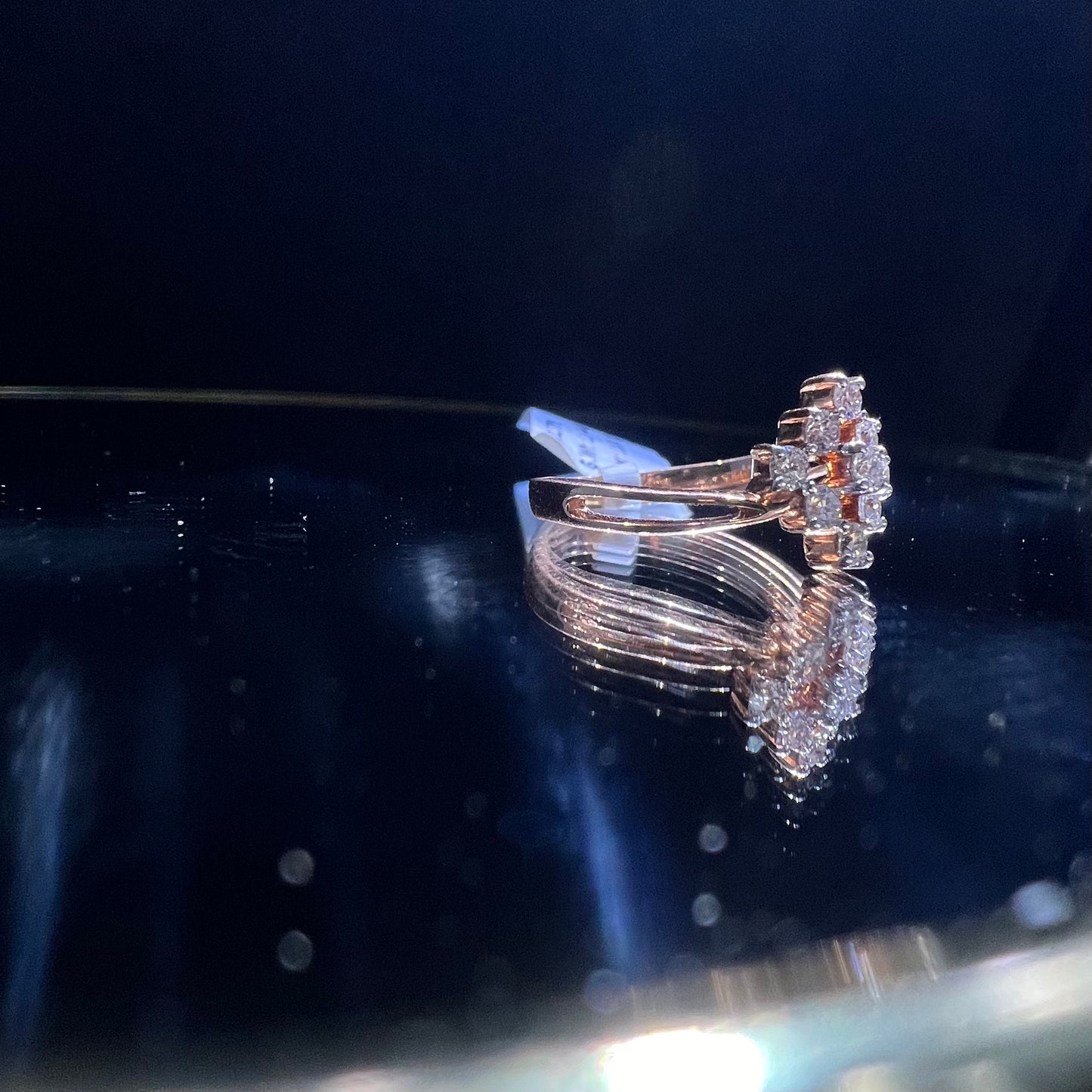 A handcrafted natural diamond solid gold ring, held on a reflective surface, showcasing the ring's design and the shine of the diamonds.