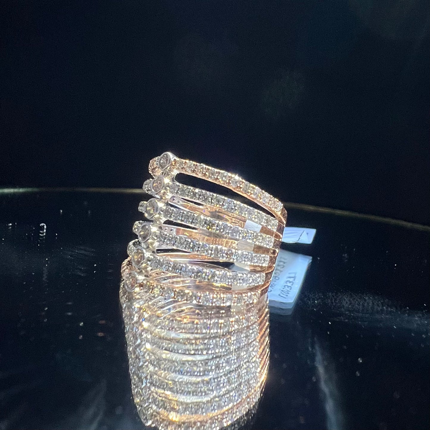 Close-up of a modern multi-band diamond ring featuring parallel pavé-set rows connected by bezel-set round diamonds, crafted in gold and reflecting light beautifully, displayed on a reflective surface.
