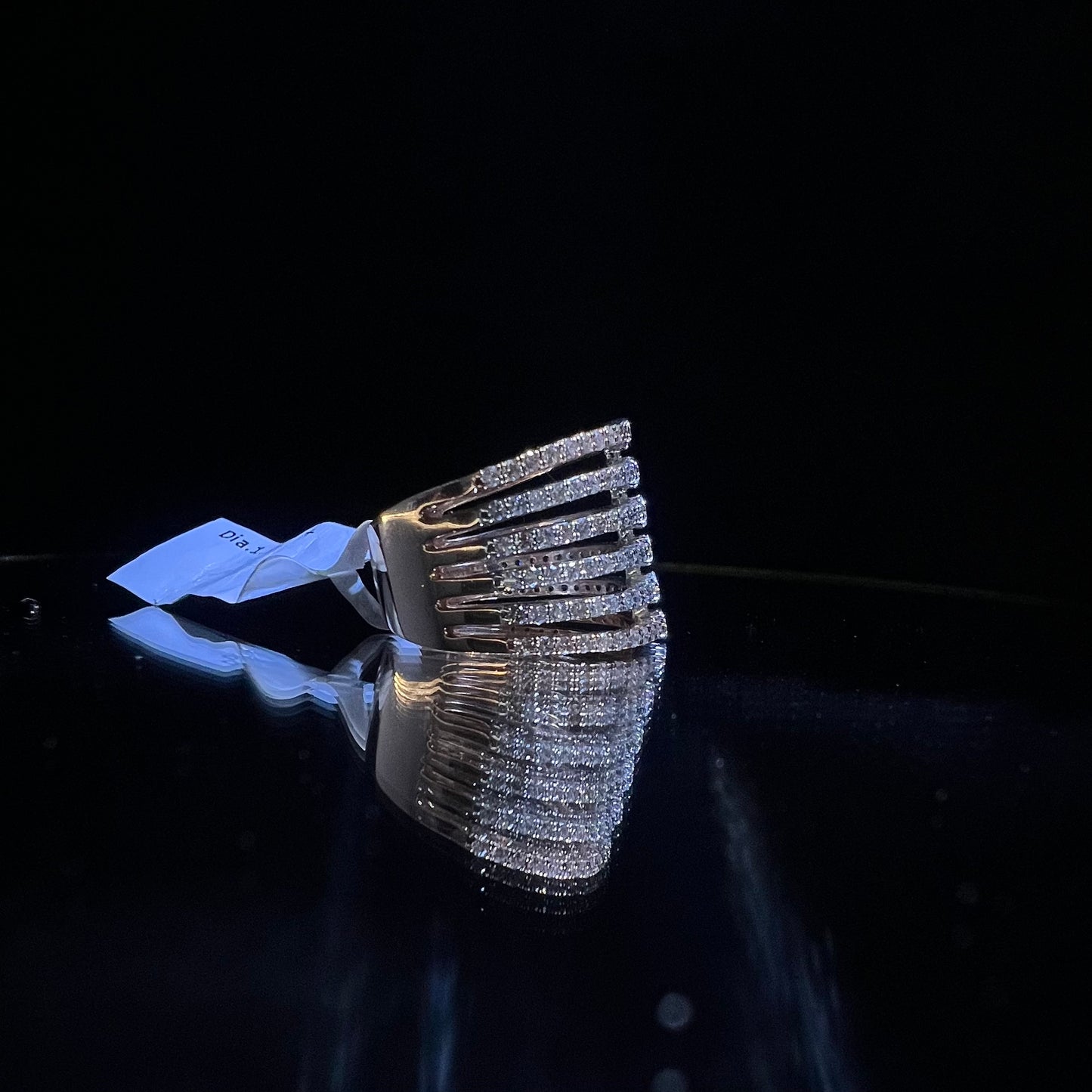 Close-up of a modern multi-band diamond ring featuring parallel pavé-set rows connected by bezel-set round diamonds, crafted in gold and reflecting light beautifully, displayed on a reflective surface.