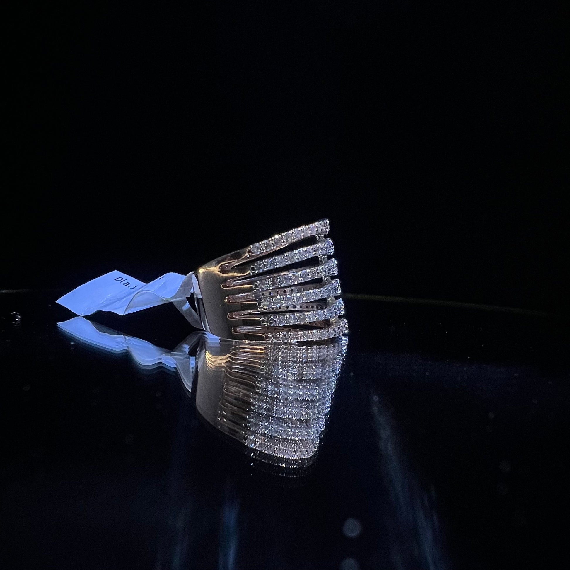 Close-up of a modern multi-band diamond ring featuring parallel pavé-set rows connected by bezel-set round diamonds, crafted in gold and reflecting light beautifully, displayed on a reflective surface.