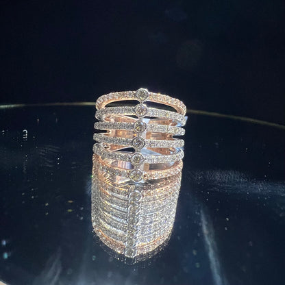 Close-up of a modern multi-band diamond ring featuring parallel pavé-set rows connected by bezel-set round diamonds, crafted in gold and reflecting light beautifully, displayed on a reflective surface.