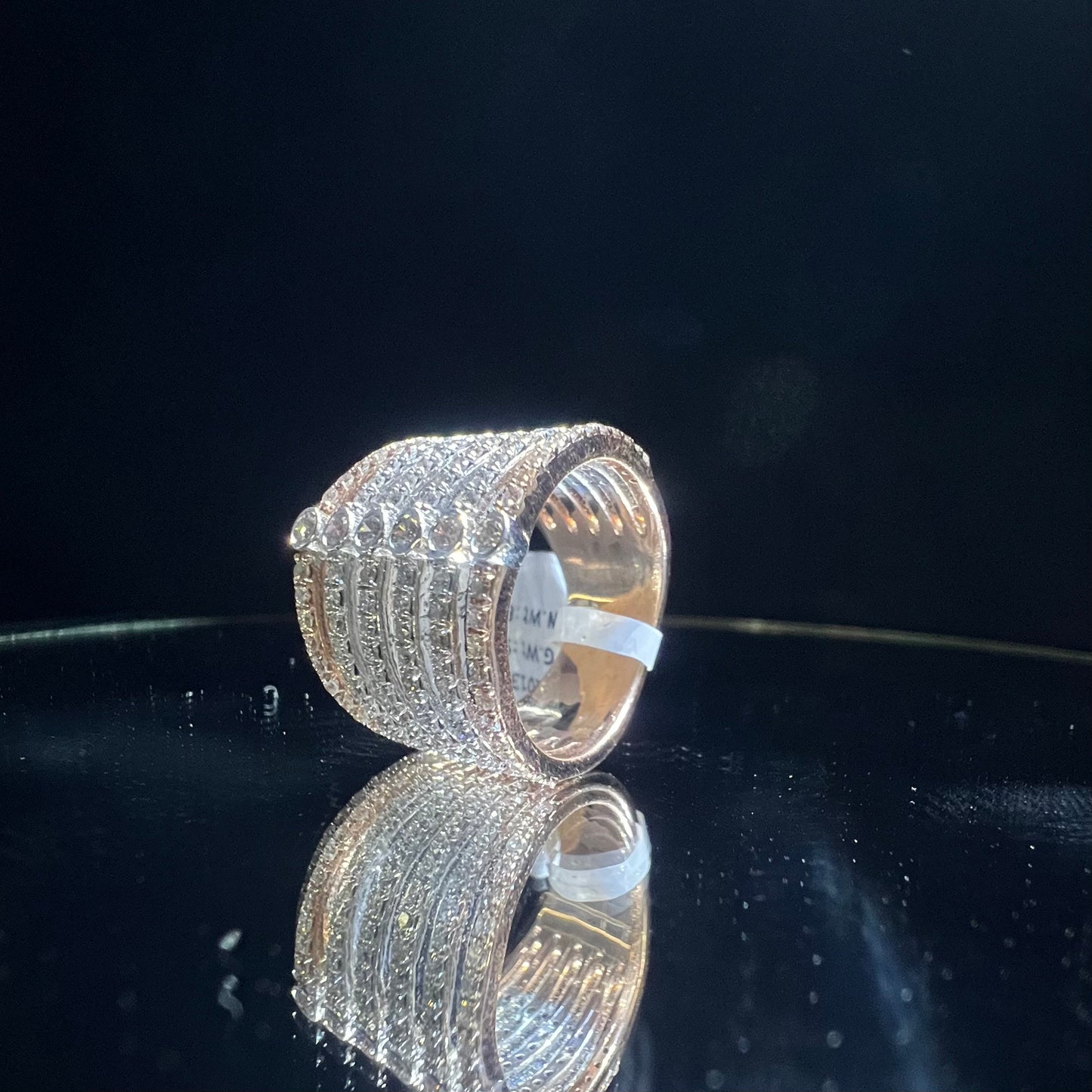 Close-up of a modern multi-band diamond ring featuring parallel pavé-set rows connected by bezel-set round diamonds, crafted in gold and reflecting light beautifully, displayed on a reflective surface.