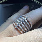 Close-up of a hand wearing a modern multi-band diamond ring featuring parallel pavé-set rows connected by bezel-set round diamonds, crafted in gold and reflecting light beautifully.