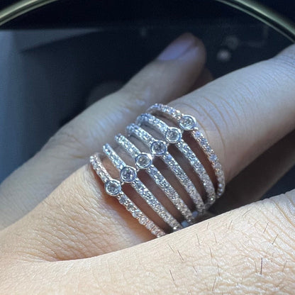 Close-up of a hand wearing a modern multi-band diamond ring featuring parallel pavé-set rows connected by bezel-set round diamonds, crafted in gold and reflecting light beautifully.