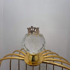 Close-up of a crown-inspired diamond ring featuring multiple baguette-shaped diamonds set upright along the top, paired with a pavé-set band in gold, displayed a glass ball that is on a gold color cage.