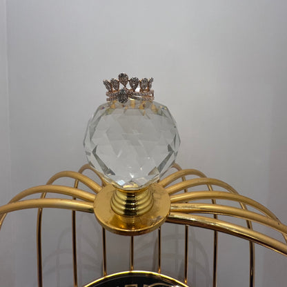 Close-up of a crown-inspired diamond ring featuring multiple baguette-shaped diamonds set upright along the top, paired with a pavé-set band in gold, displayed a glass ball that is on a gold color cage.
