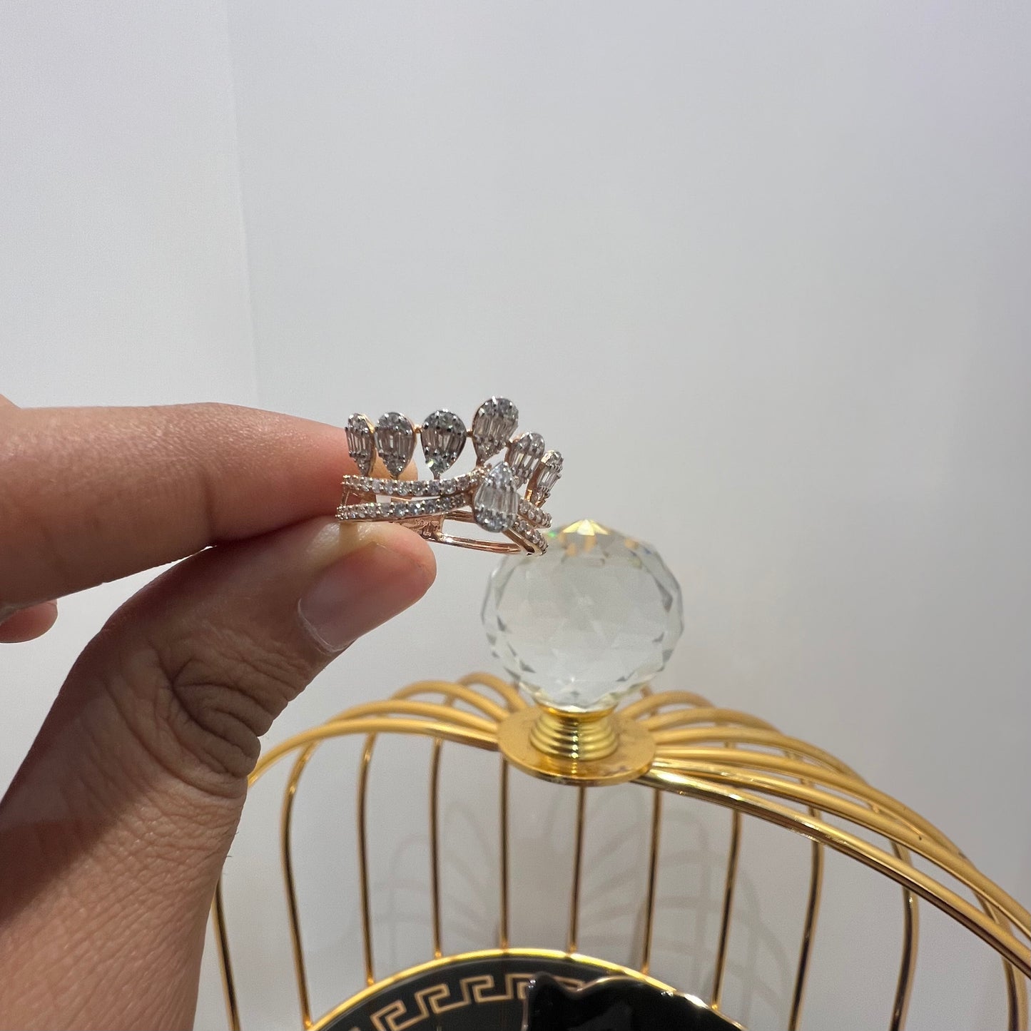 Close-up of a hand holding a crown-inspired diamond ring featuring multiple baguette-shaped diamonds set upright along the top, paired with a pavé-set band in gold, displayed against a gold color cage.