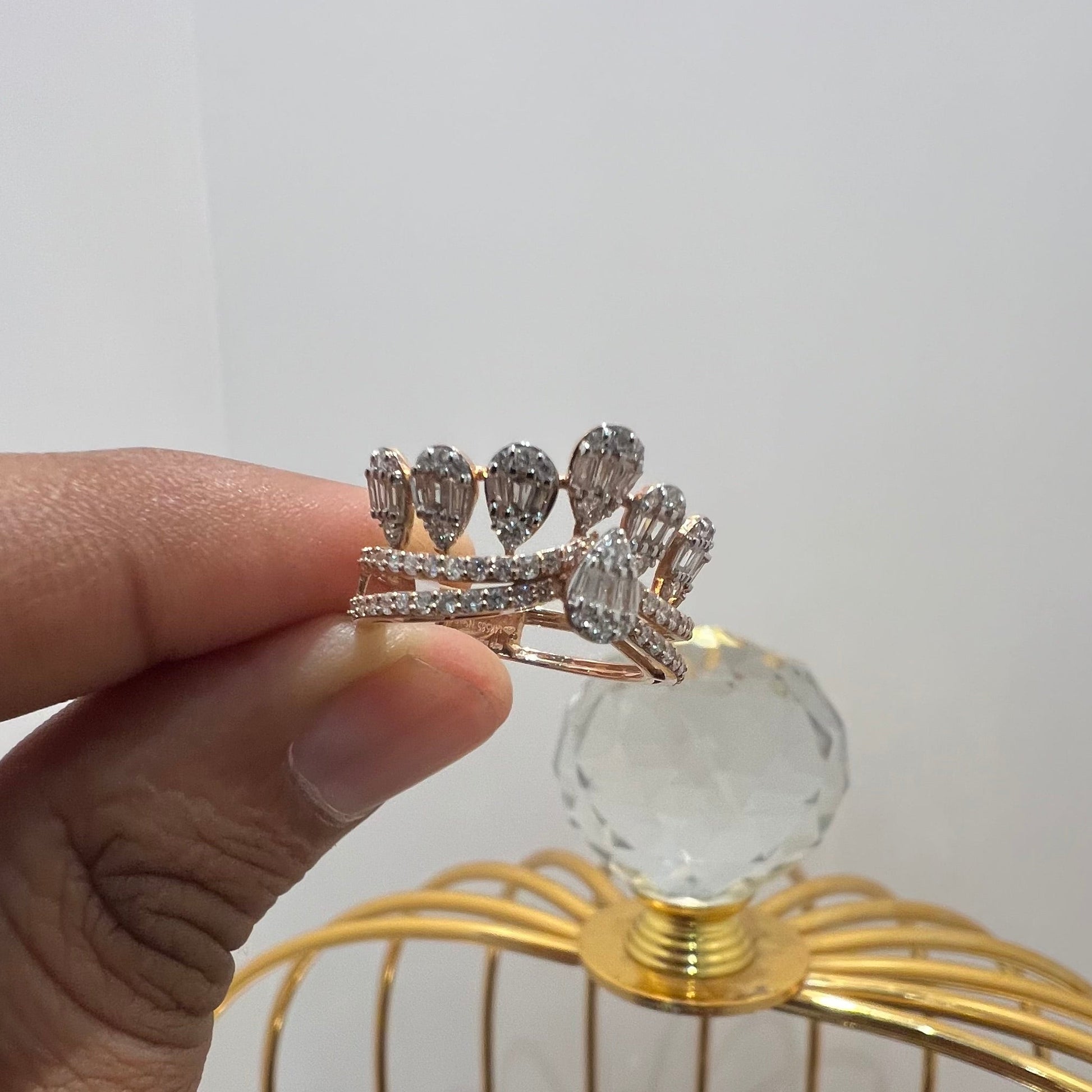 Close-up of a hand holding a crown-inspired diamond ring featuring multiple baguette-shaped diamonds set upright along the top, paired with a pavé-set band in gold, displayed against a gold color cage.