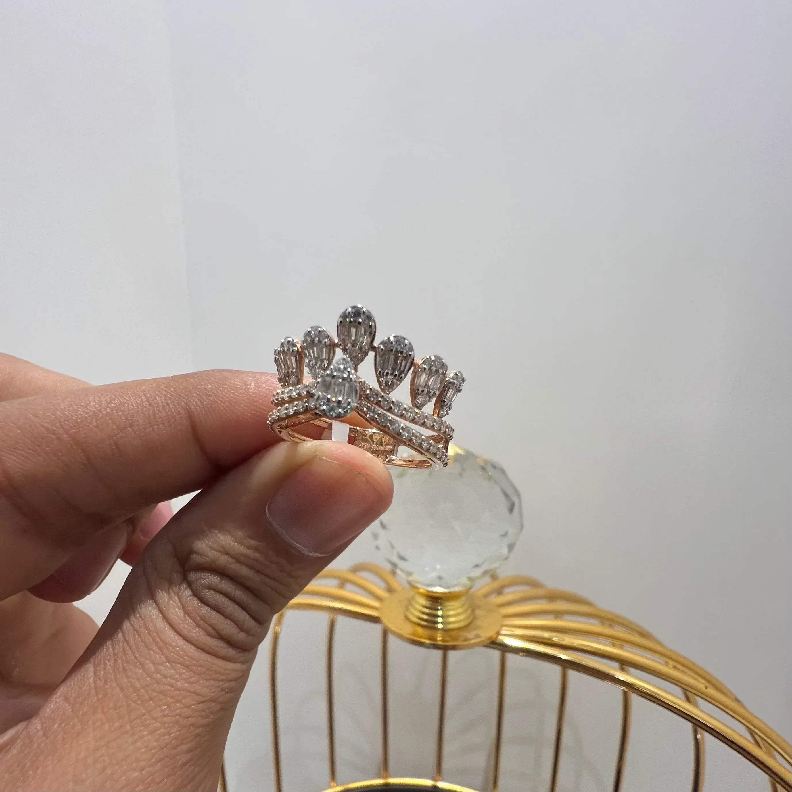 Close-up of a hand holding a crown-inspired diamond ring featuring multiple baguette-shaped diamonds set upright along the top, paired with a pavé-set band in gold, displayed against a gold color cage.
