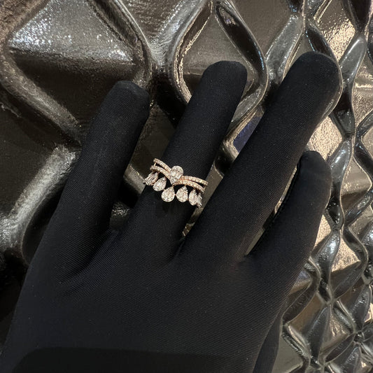 Close-up of a hand holding a crown-inspired diamond ring featuring multiple baguette-shaped diamonds set upright along the top, paired with a pavé-set band in gold, displayed against a light background with a decorative element.