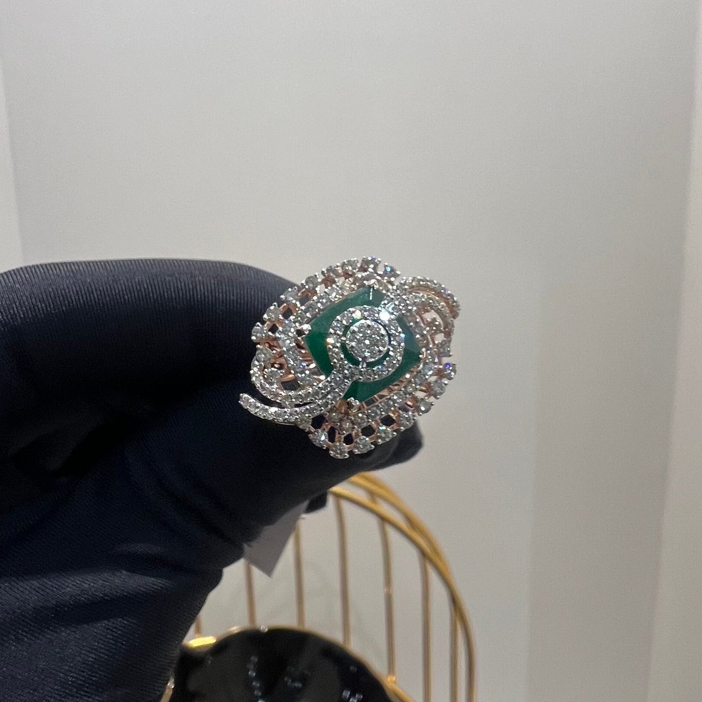 A handcrafted natural diamond solid gold ring held in a person's hand, with a green gemstone and intricate gold detailing.