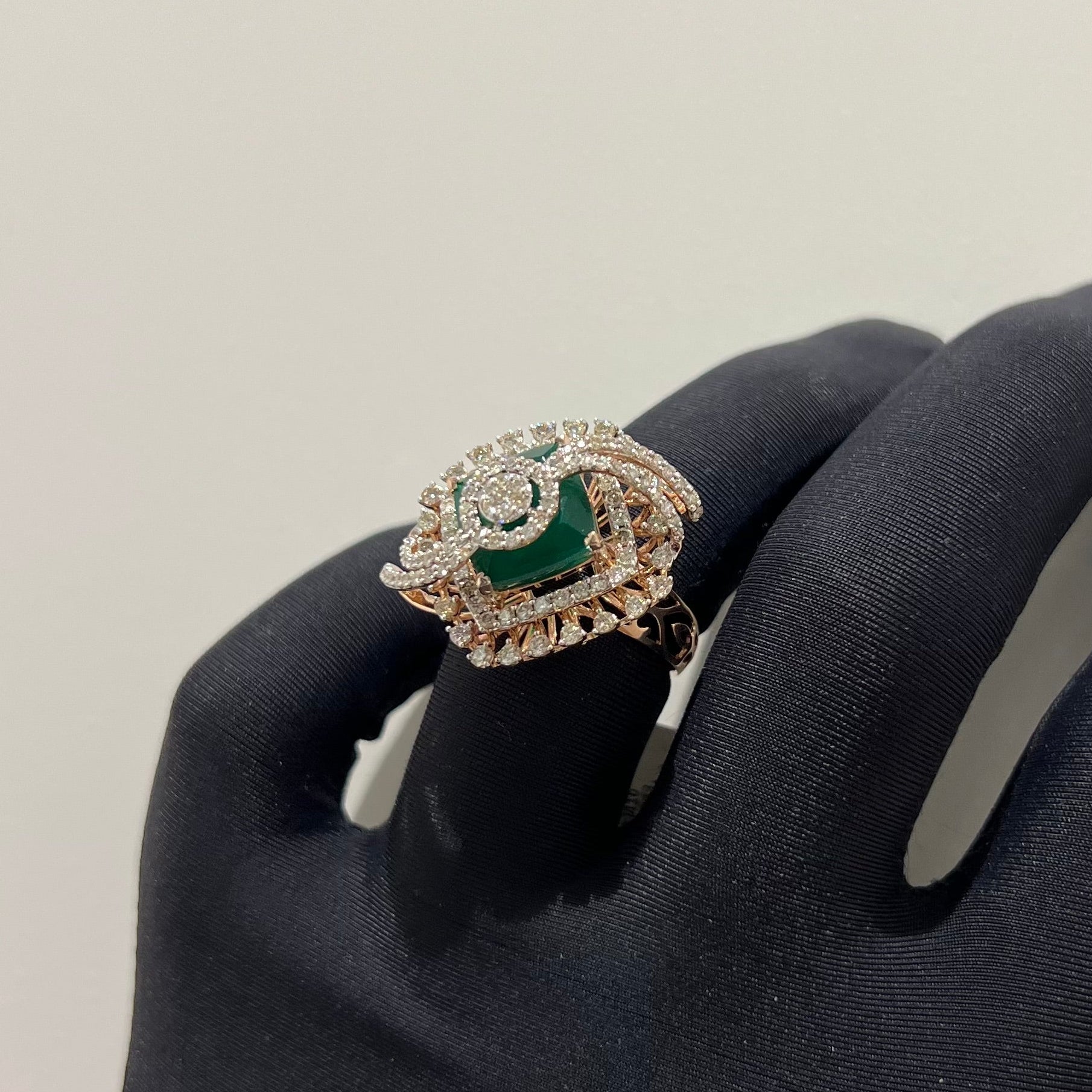 A handcrafted natural diamond solid gold ring held in a person's hand, with a green gemstone and intricate gold detailing.