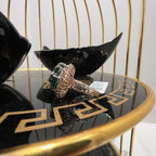 A handcrafted natural diamond solid gold ring with a green gemstone and intricate gold detailing, displayed on a black reflective surface.