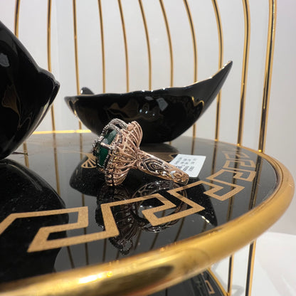 A handcrafted natural diamond solid gold ring with a green gemstone and intricate gold detailing, displayed on a black reflective surface.