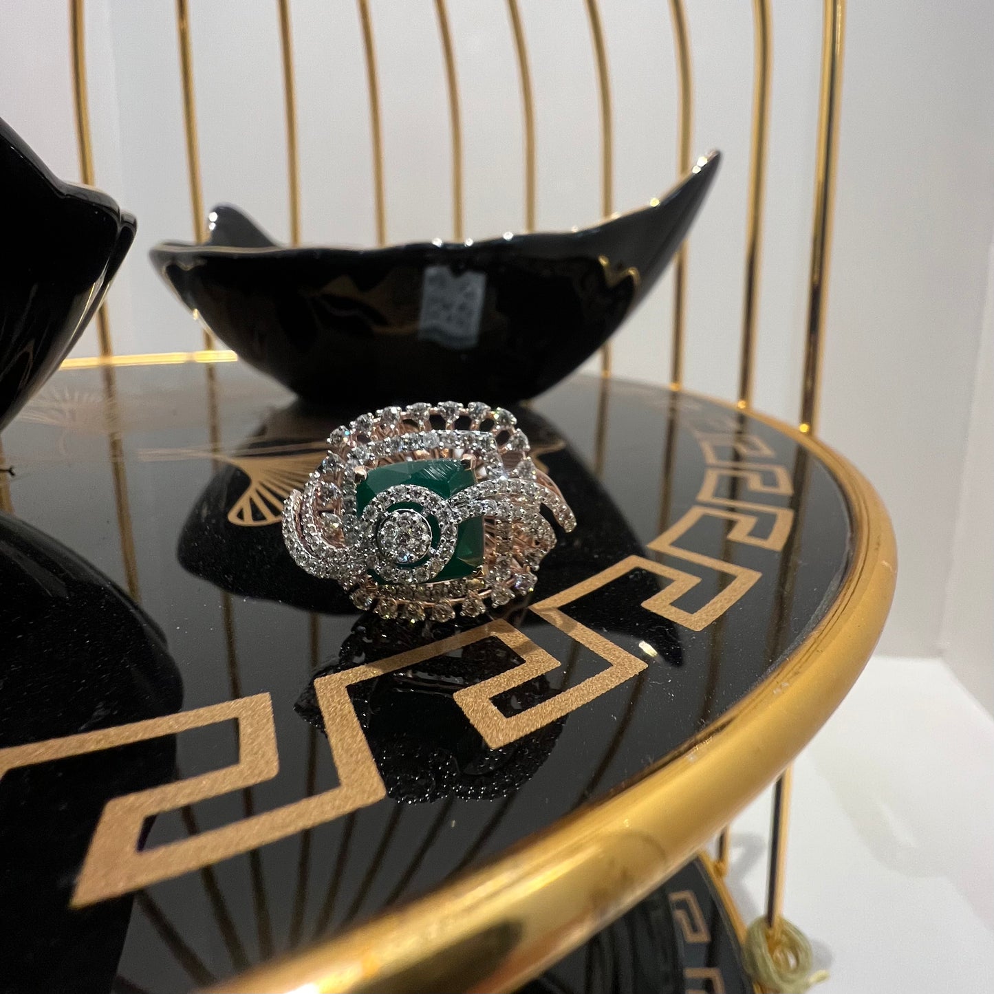 A handcrafted natural diamond solid gold ring with a green gemstone and intricate gold detailing, displayed on a black reflective surface.